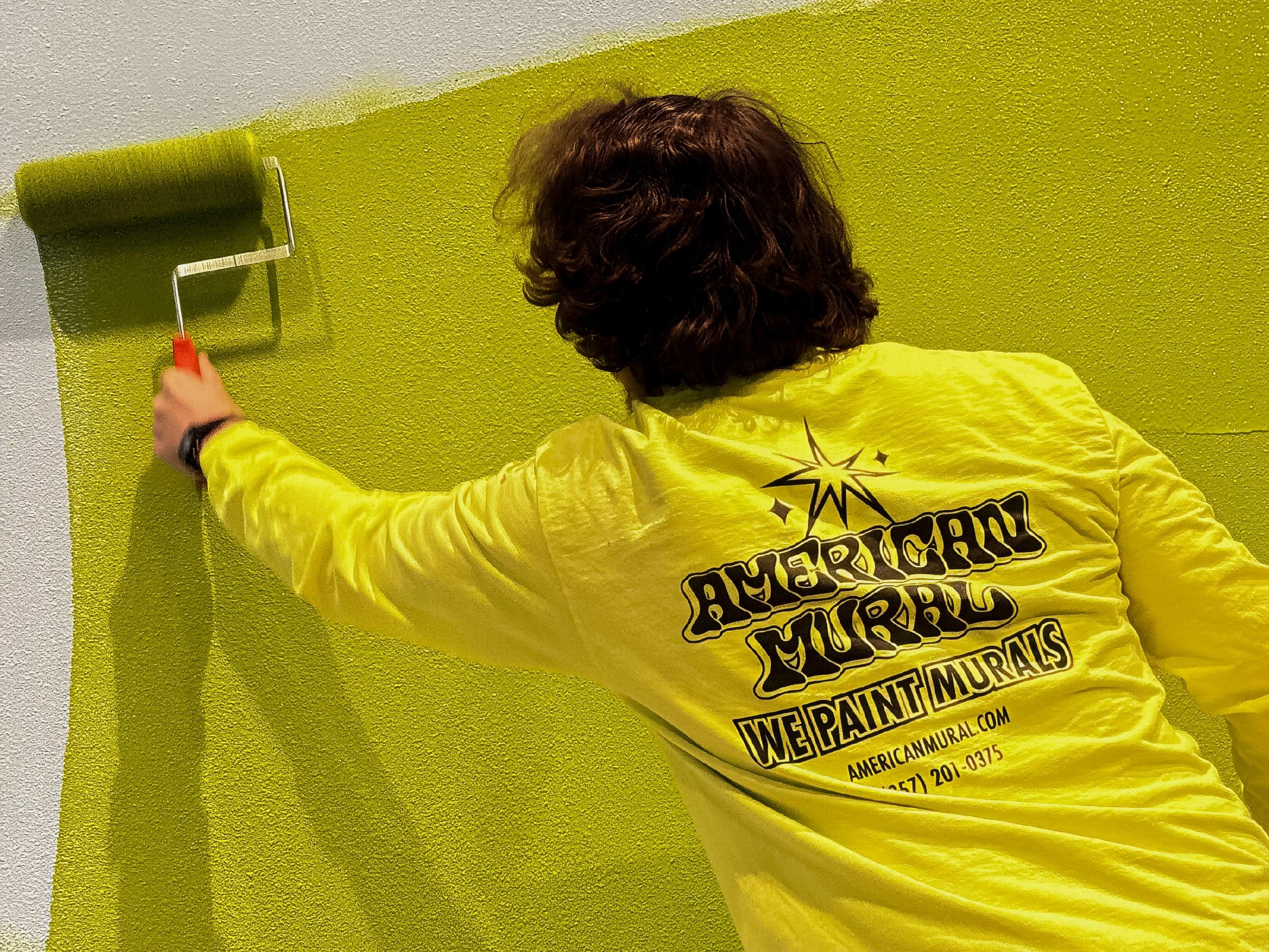 American Mural painter rolling bright green paint across a textured wall.
