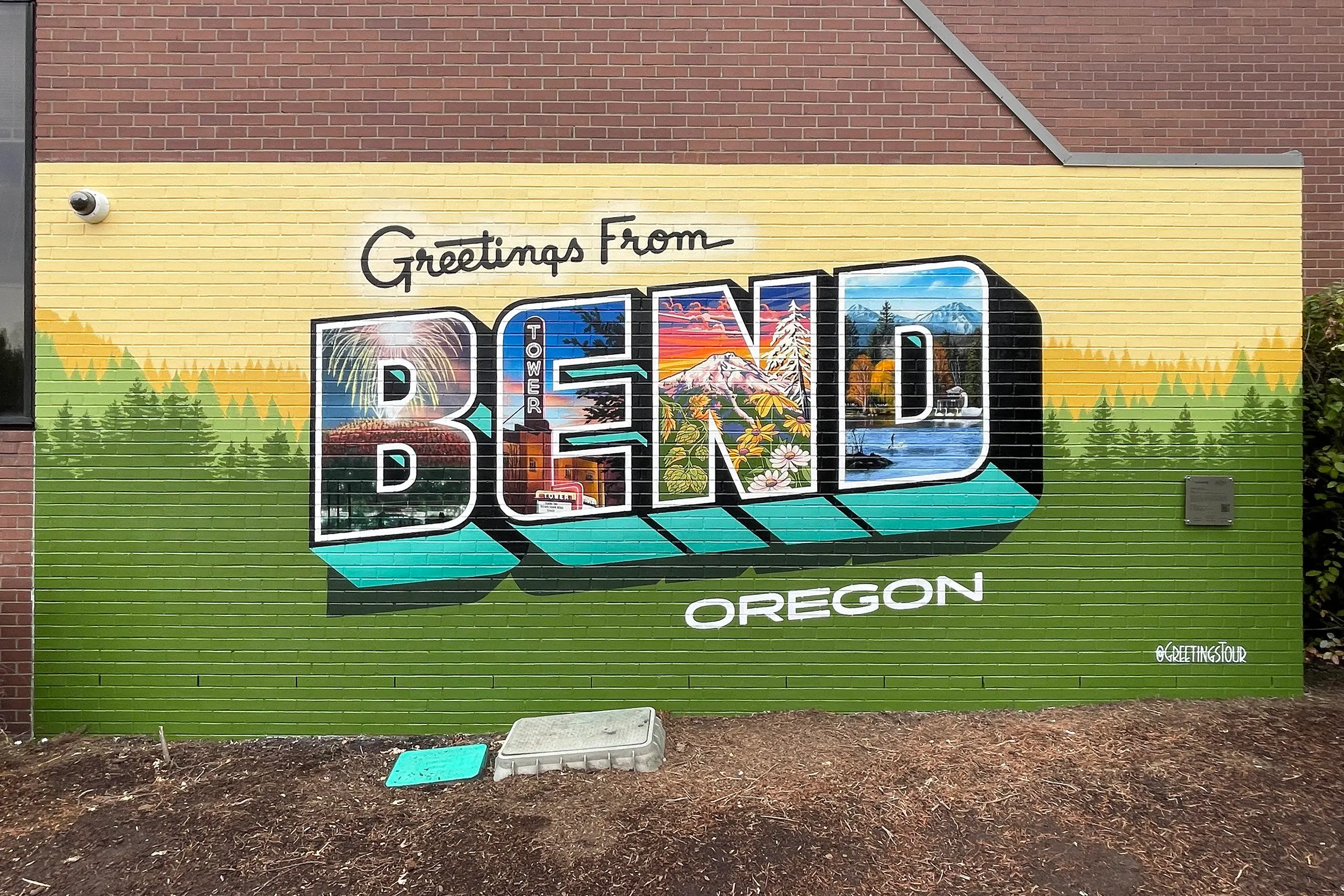 Completed Greetings from Bend postcard mural on a yellow brick wall