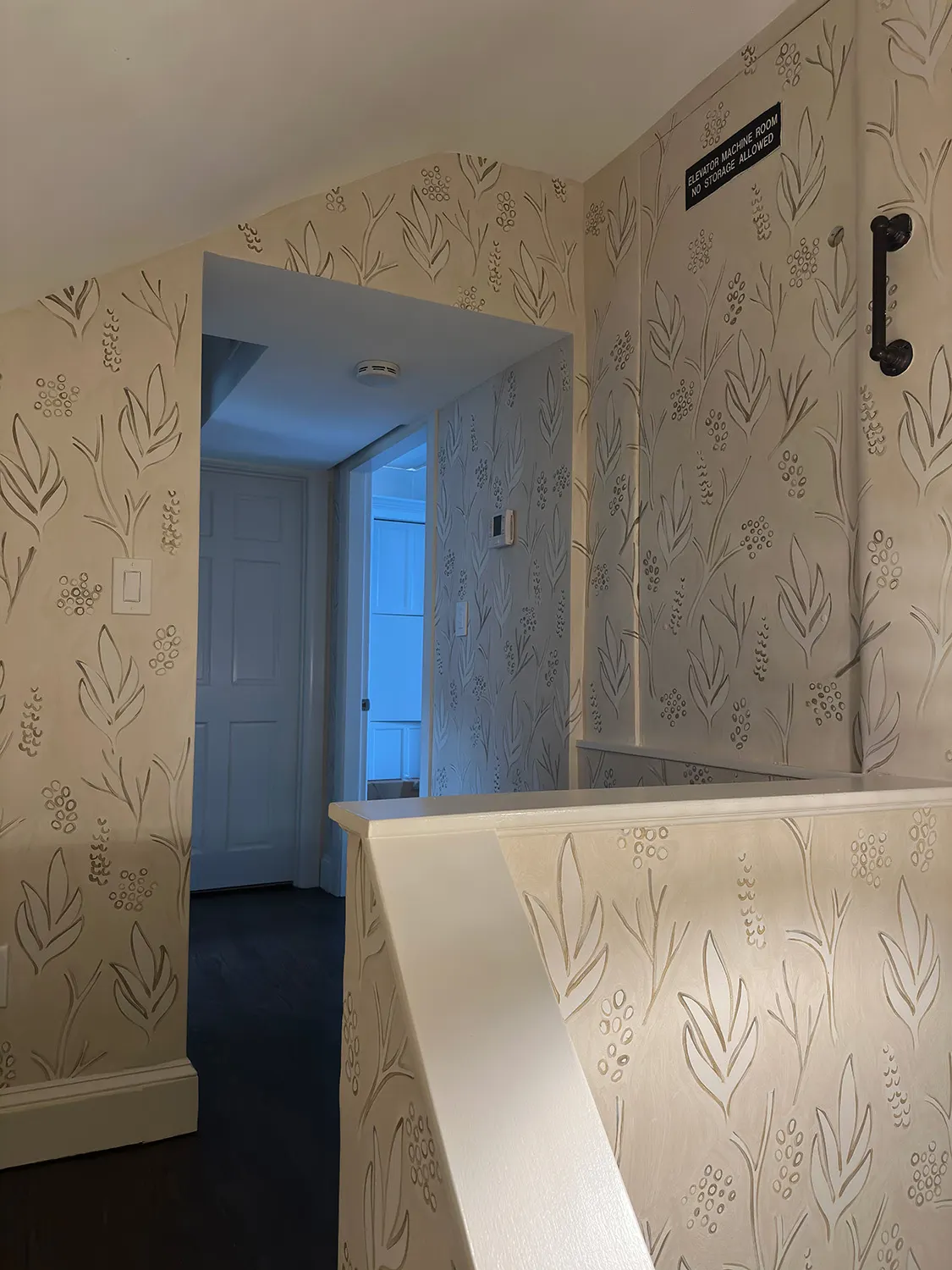 Hand-painted pattern continuing through an arched hallway beside the stairwell