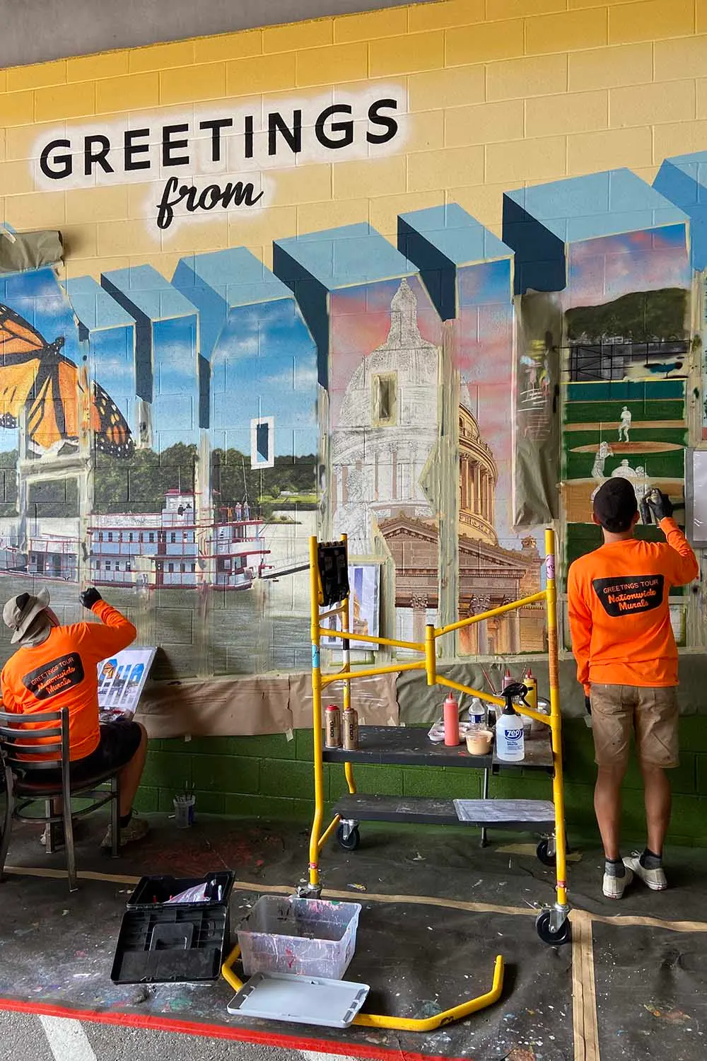 Two artists painting detailed scenes from lifts on the Charleston mural