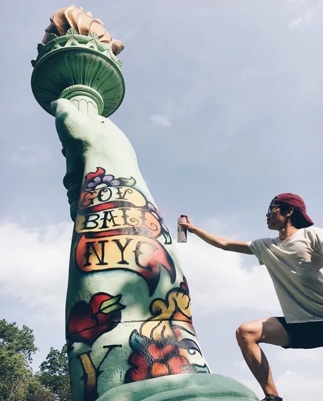 Artist spray-painting the tattooed arm of the giant GovBall Statue of Liberty beneath its raised torch