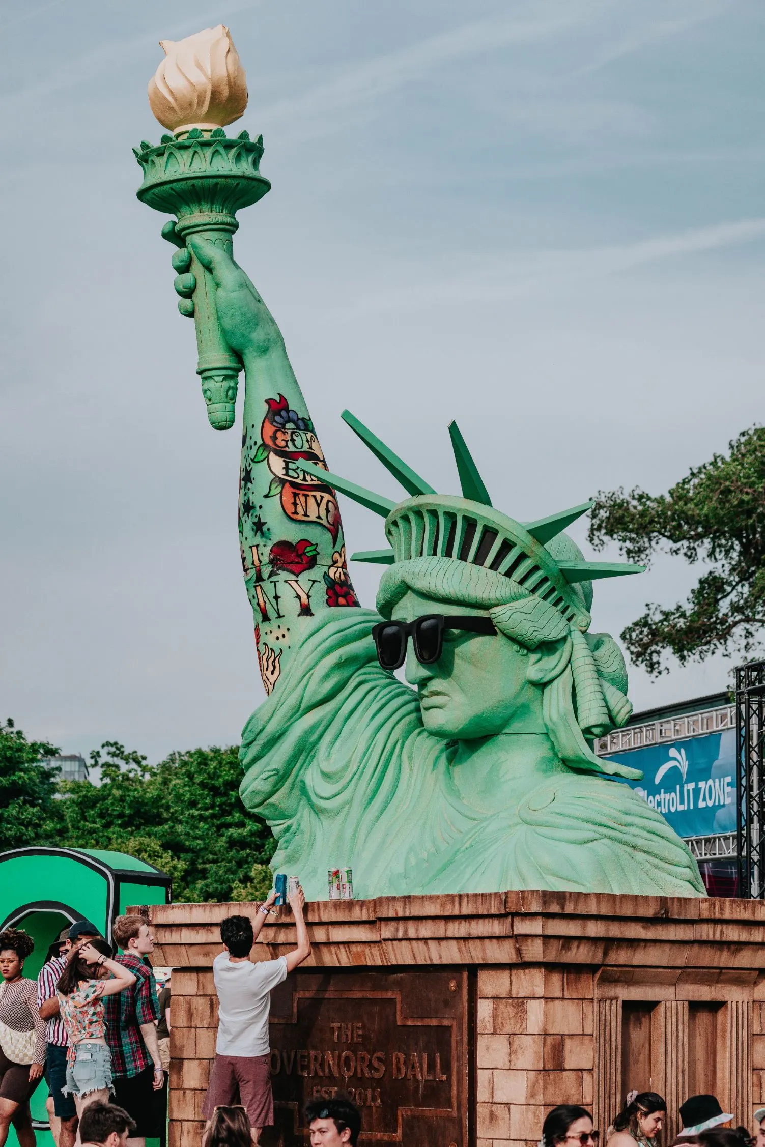 GovBall Statue of Liberty wearing black sunglasses with the finished tattoo sleeve visible above the festival crowd