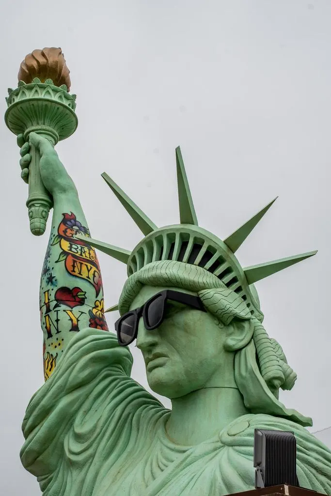 Low-angle view of the giant Statue of Liberty sculpture wearing sunglasses with its tattooed arm raised
