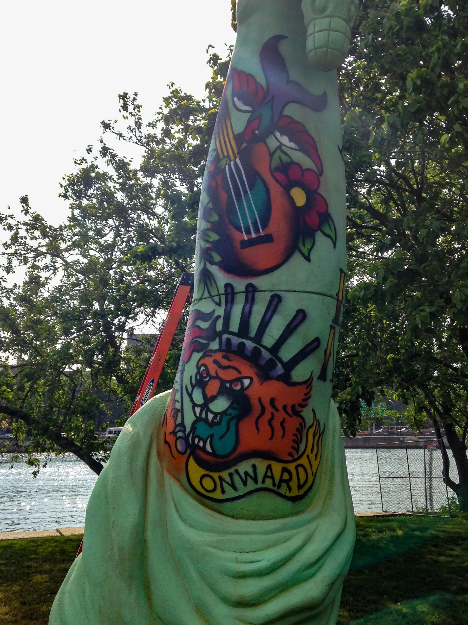 Close view of American traditional guitar and tiger tattoos wrapping the Statue of Liberty sculpture's arm