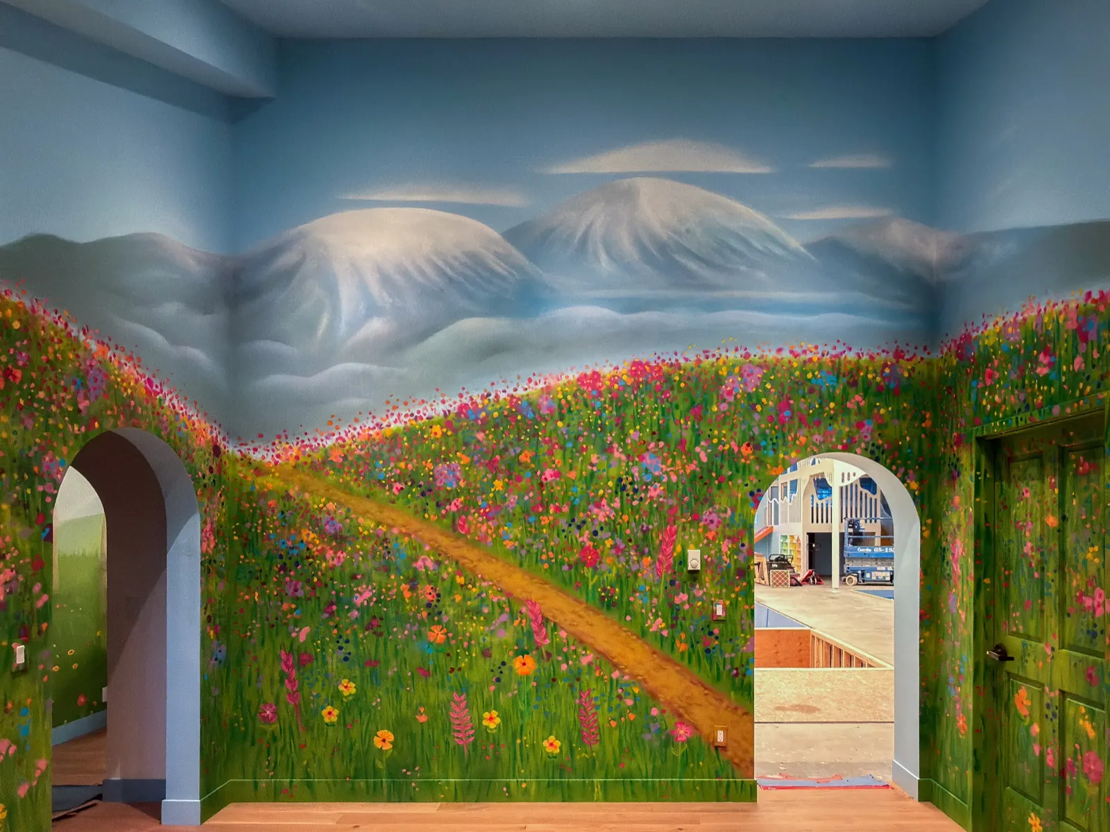 Mountain-and-wildflower mural spanning the playroom wall between two rounded archways