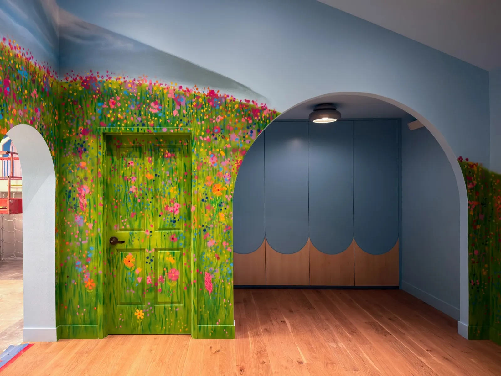 Green playroom door painted into a colorful wildflower meadow beside a large arched nook