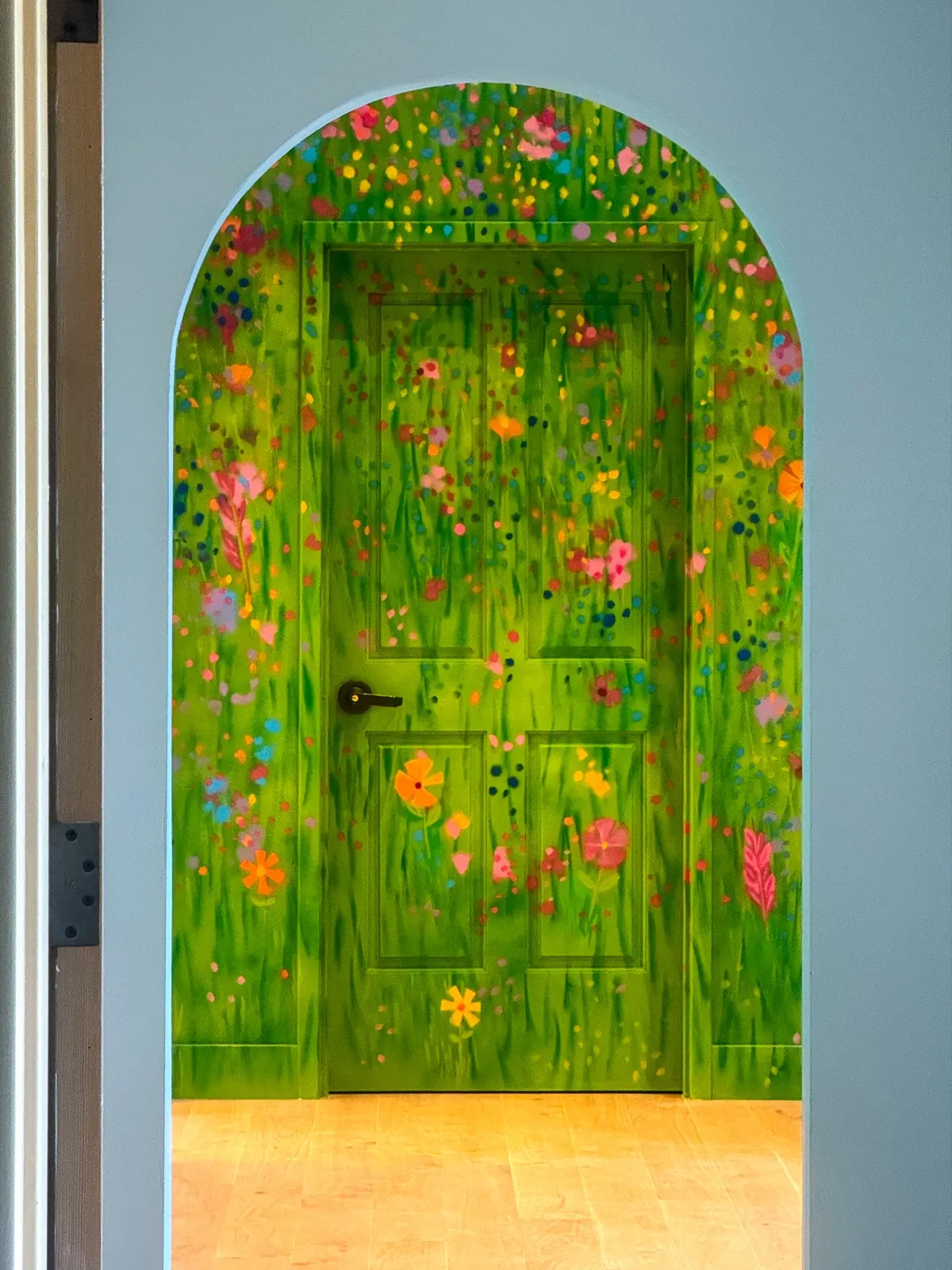 Wildflower-painted green door framed by a rounded opening in the playroom