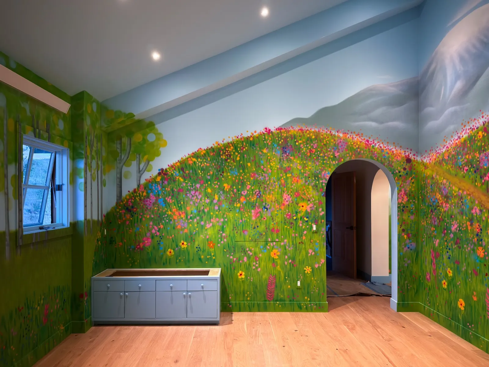 Playroom mural wrapping flowered hills, white-trunked trees, a mountain peak, a window, and an arched doorway