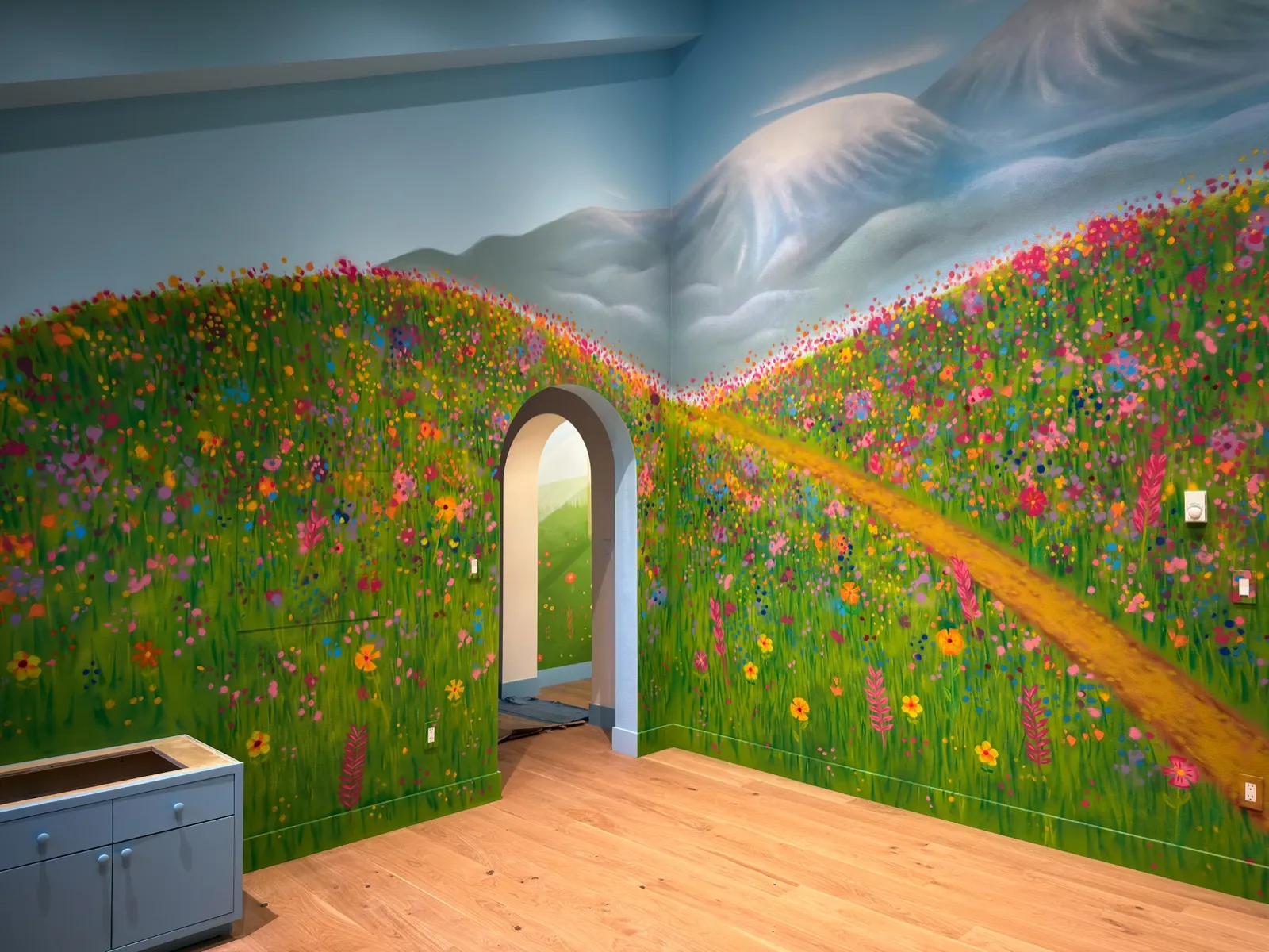 Wide view of flowered hills and a winding trail meeting snowy mountains across a playroom corner