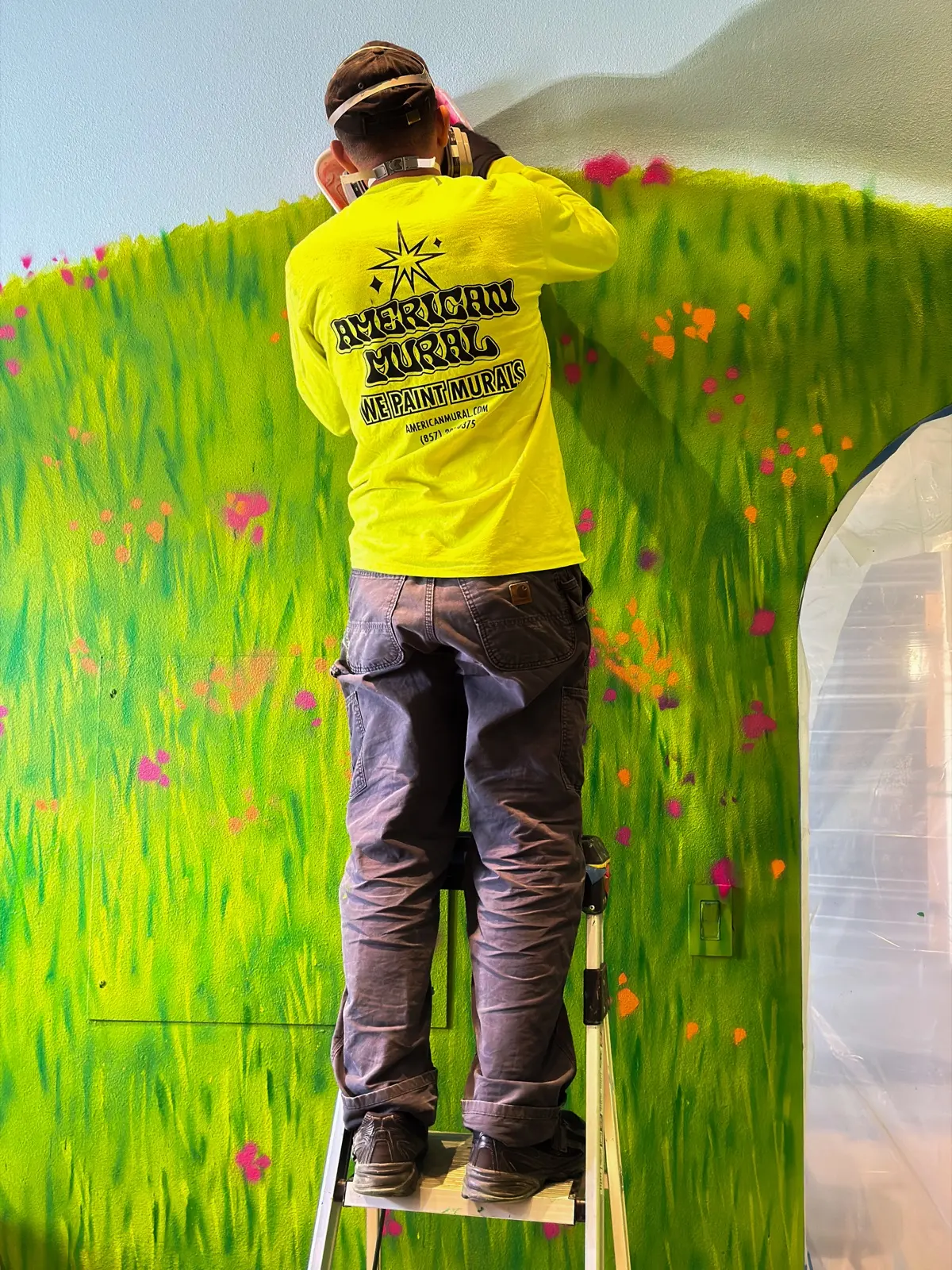 American Mural painter working from a stepladder on meadow details above an arched opening.