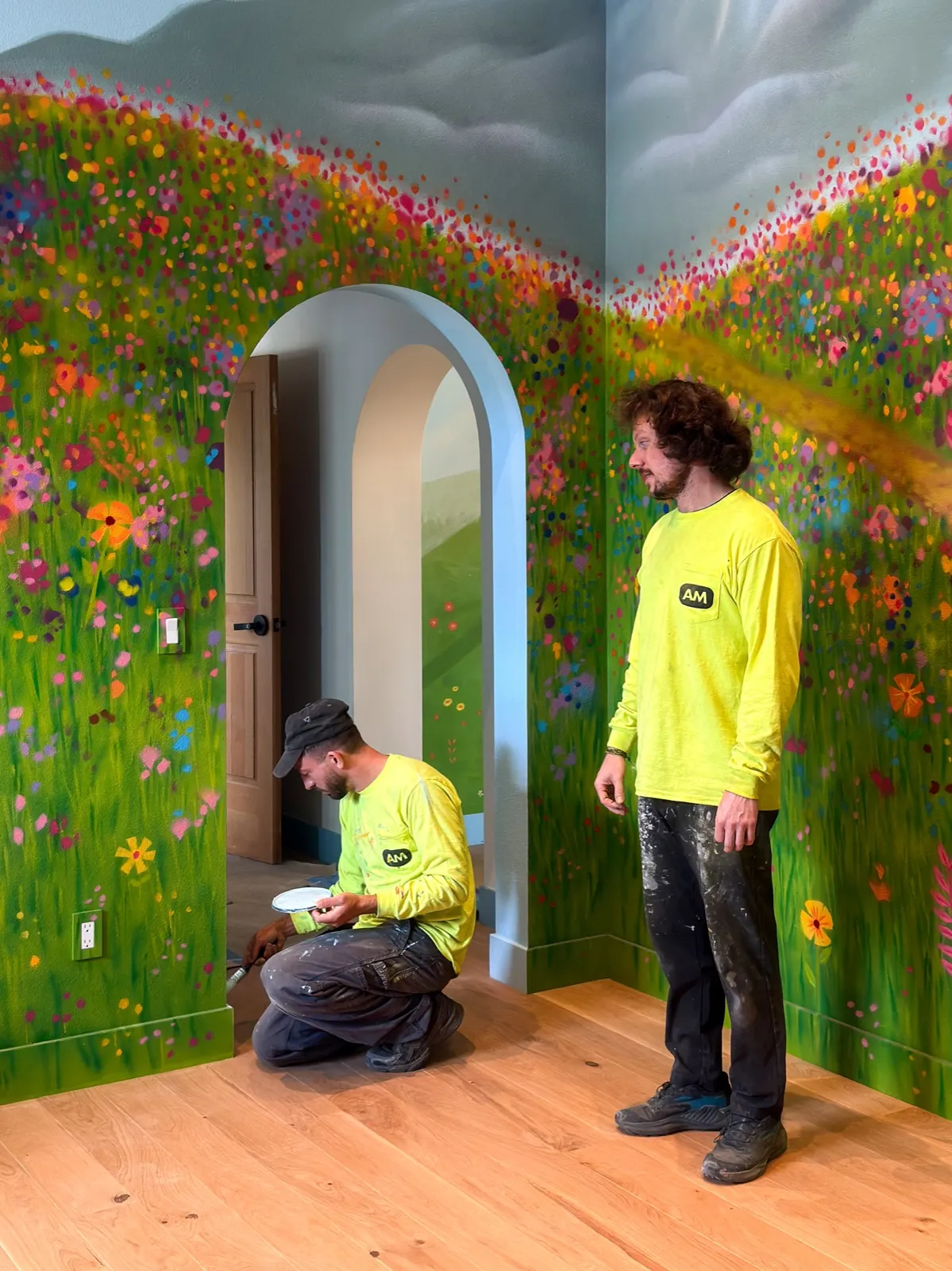 Two American Mural painters adding finishing details inside the wildflower-and-mountain playroom