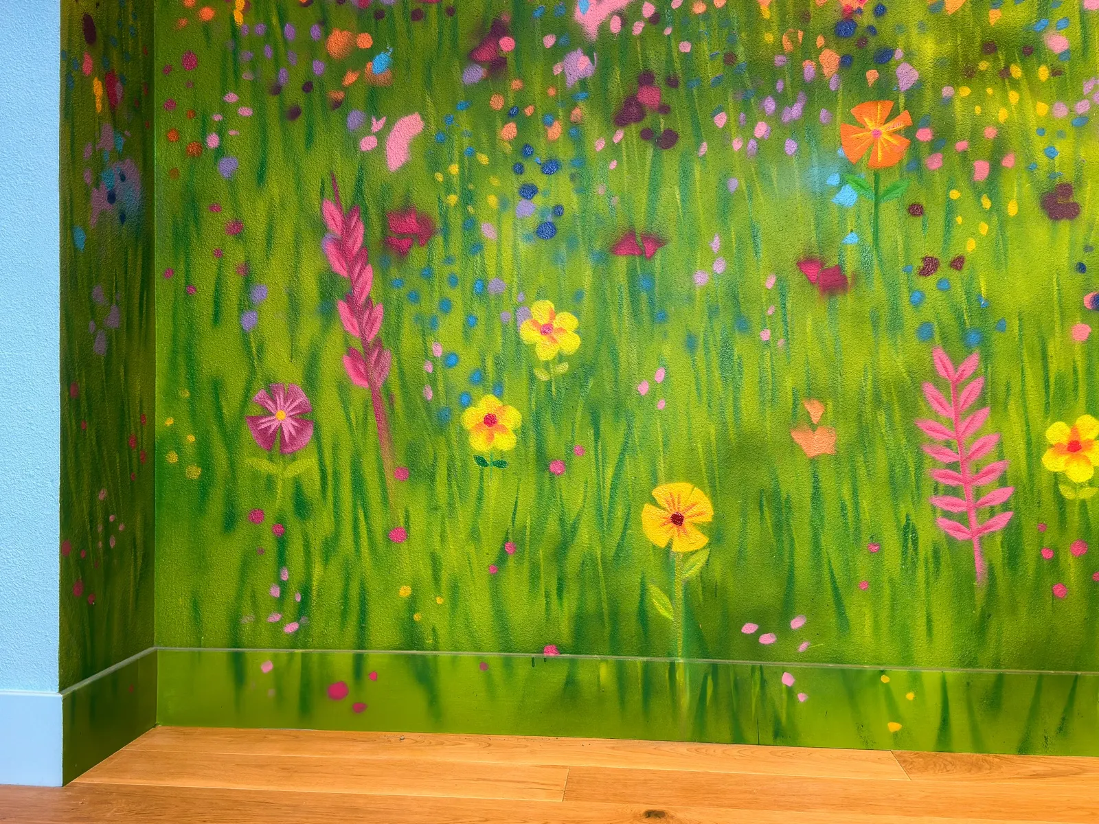 Close view of painted grass, leaves, and colorful wildflowers continuing across the baseboard