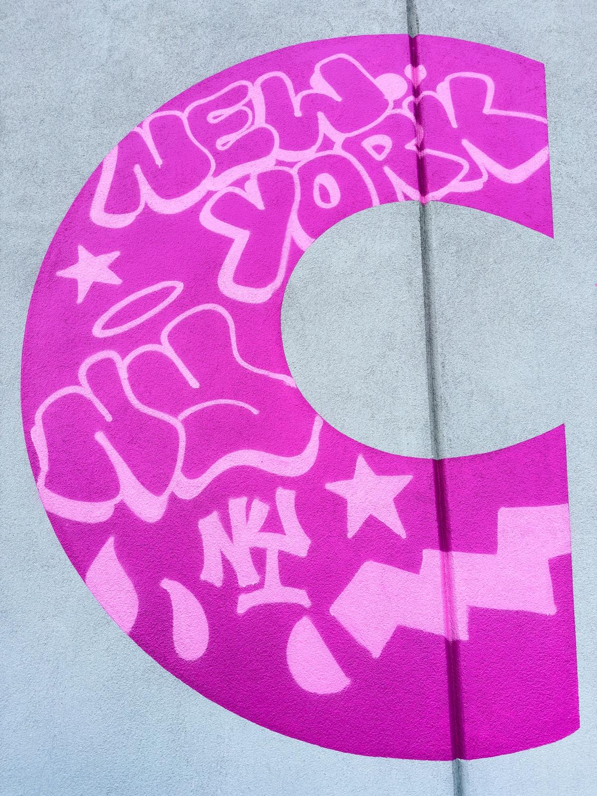 Close view of the pink letter C filled with pale graffiti tags, stars, drips, and New York details
