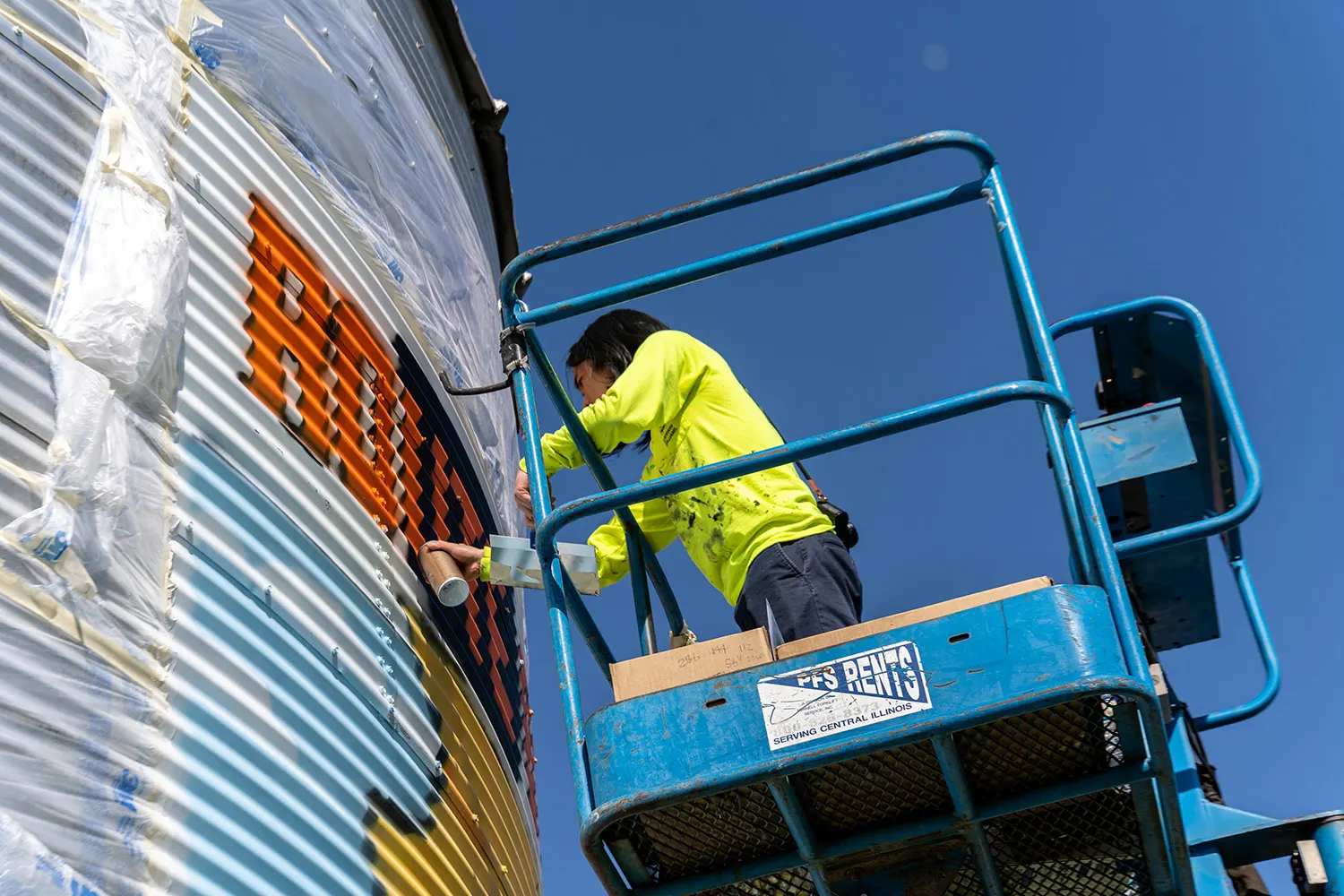 Artist spray-painting around the silo's rivets and curved surface
