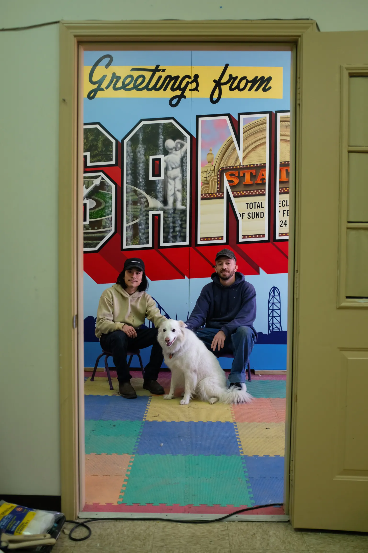 Two artists and a white dog in front of the Sandusky panels during production