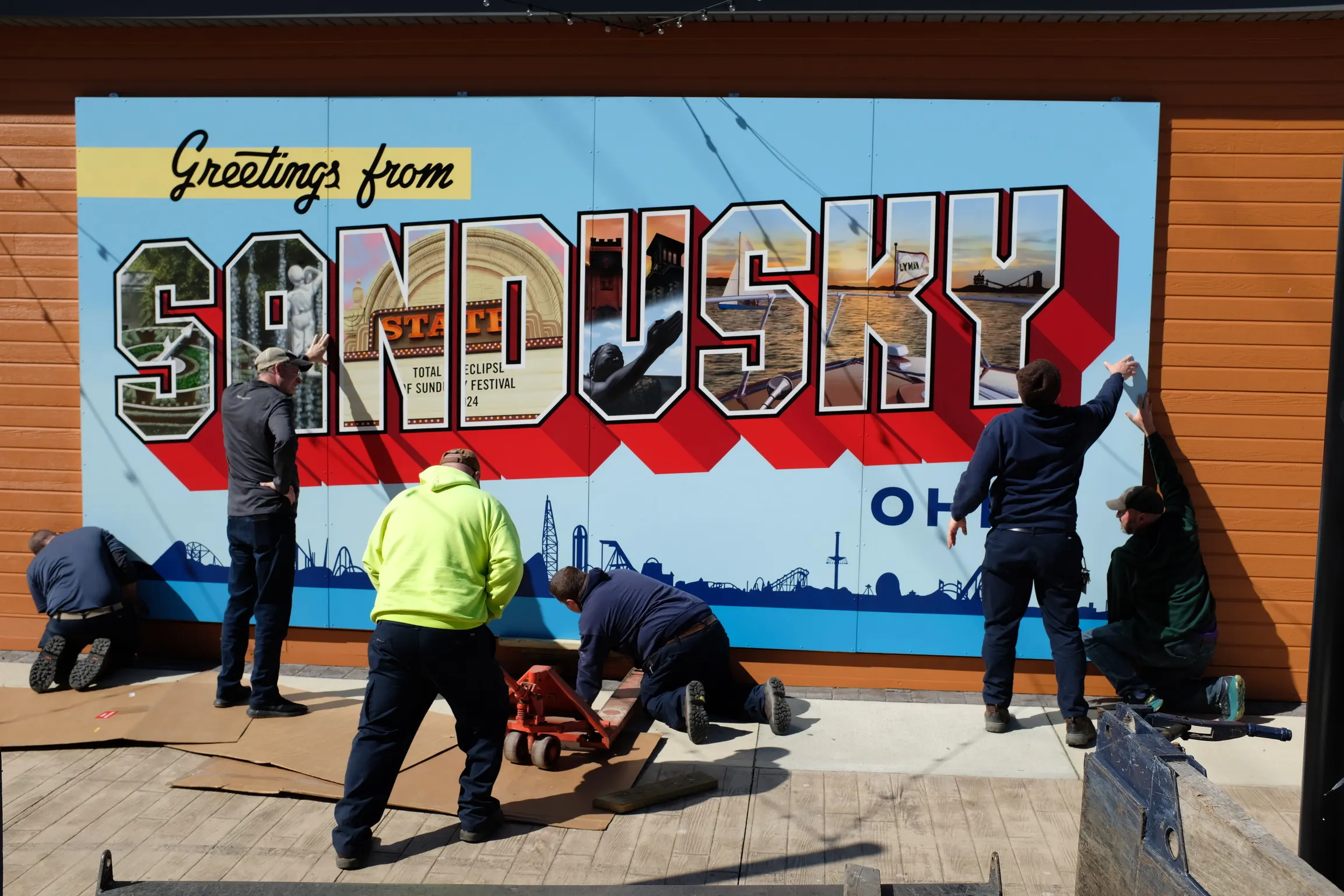Installation crew positioning the completed Sandusky mural outdoors