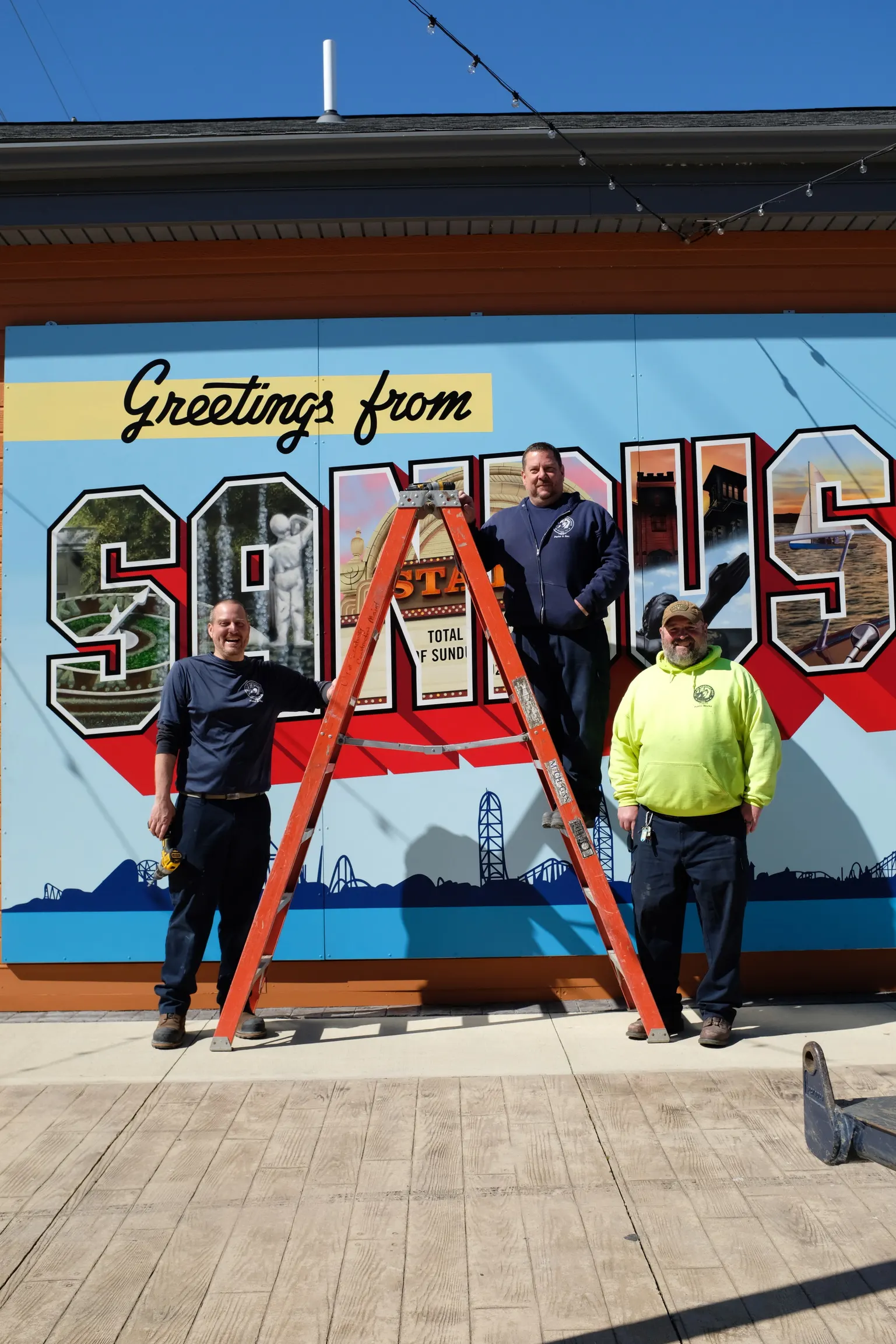 Three installers standing with the completed Greetings from Sandusky mural