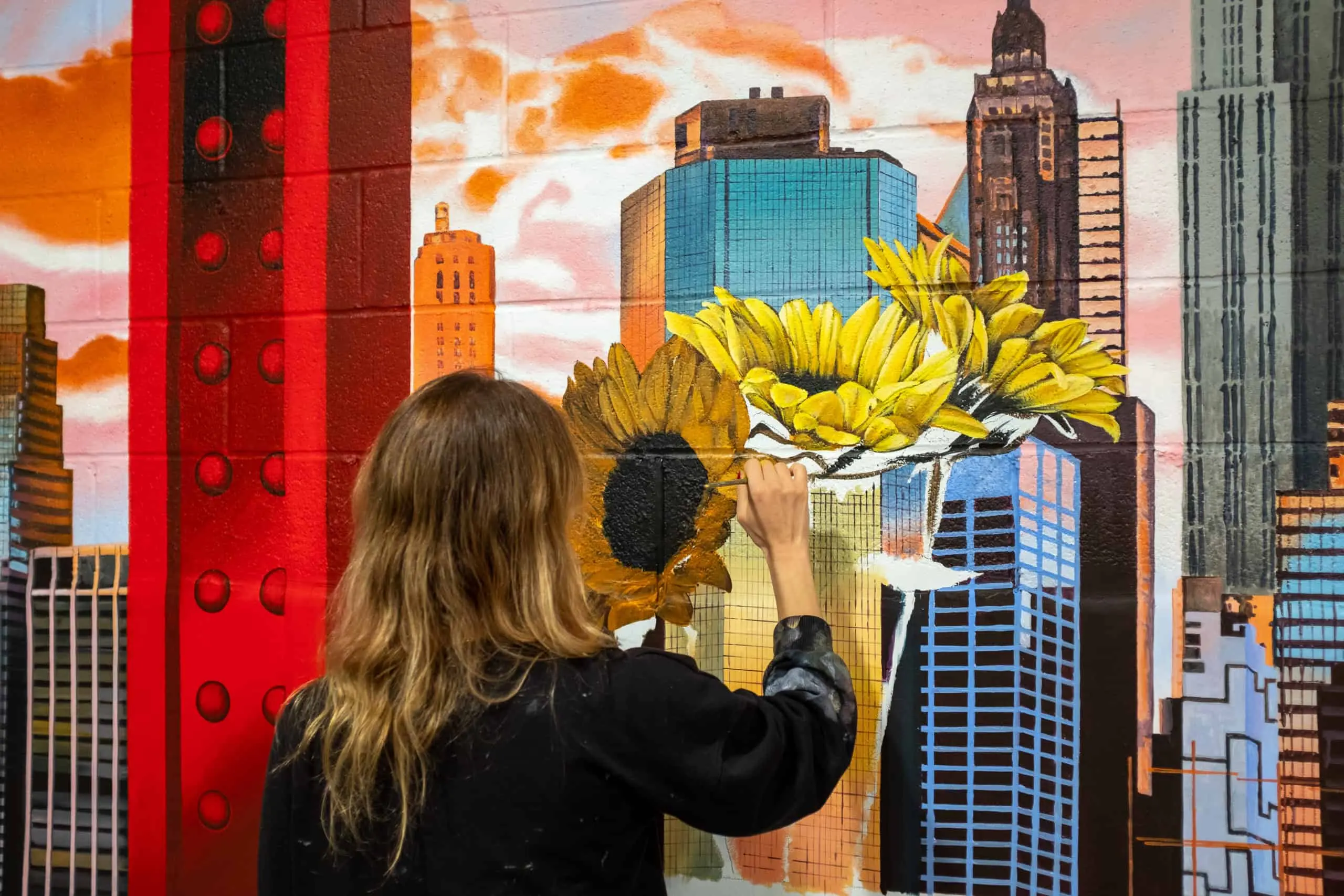 Artist brush-painting sunflowers against the New York skyline inside the Waterline Square skatepark.
