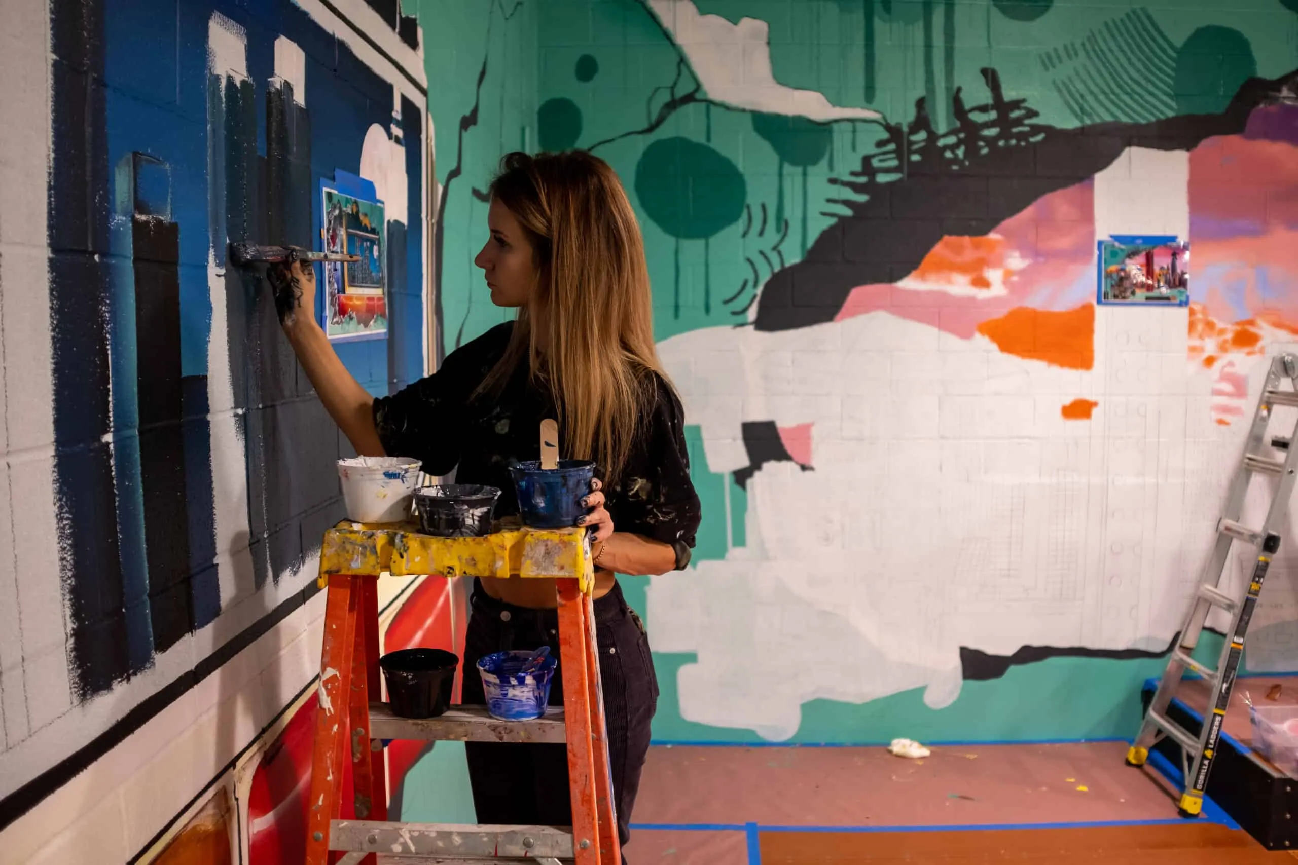 Artist painting a dark skyline panel inside the skatepark