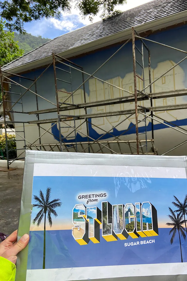 Printed St. Lucia mural plan held in front of the scaffolded wall