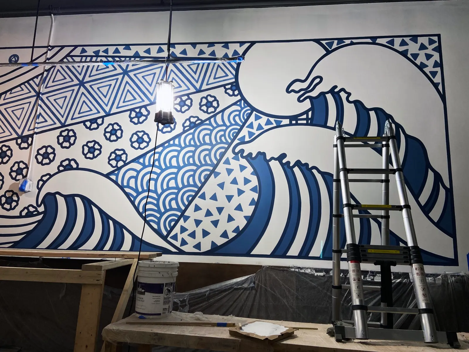 Right side of the indigo Sugidama mural with layered waves and geometric patterns during installation