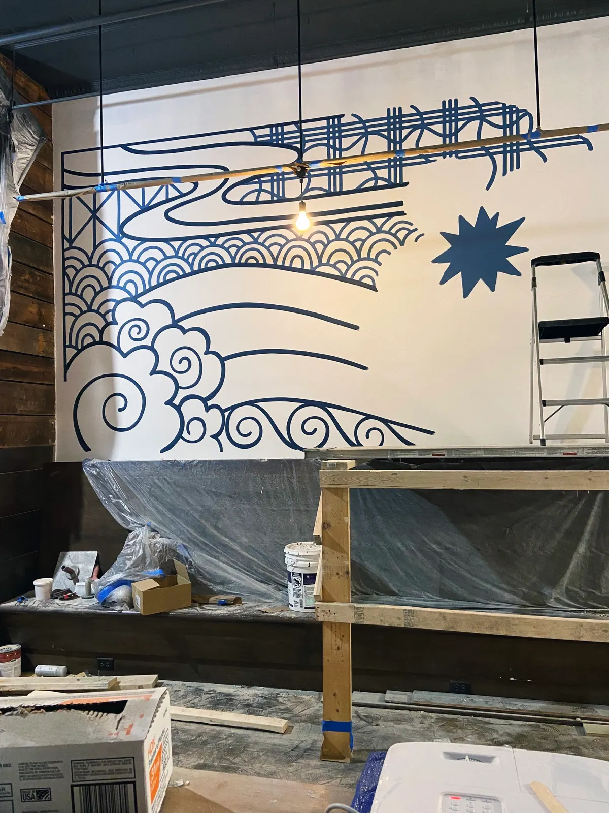 Left side of the Sugidama mural in progress with indigo outlines of waves and tile-inspired patterns
