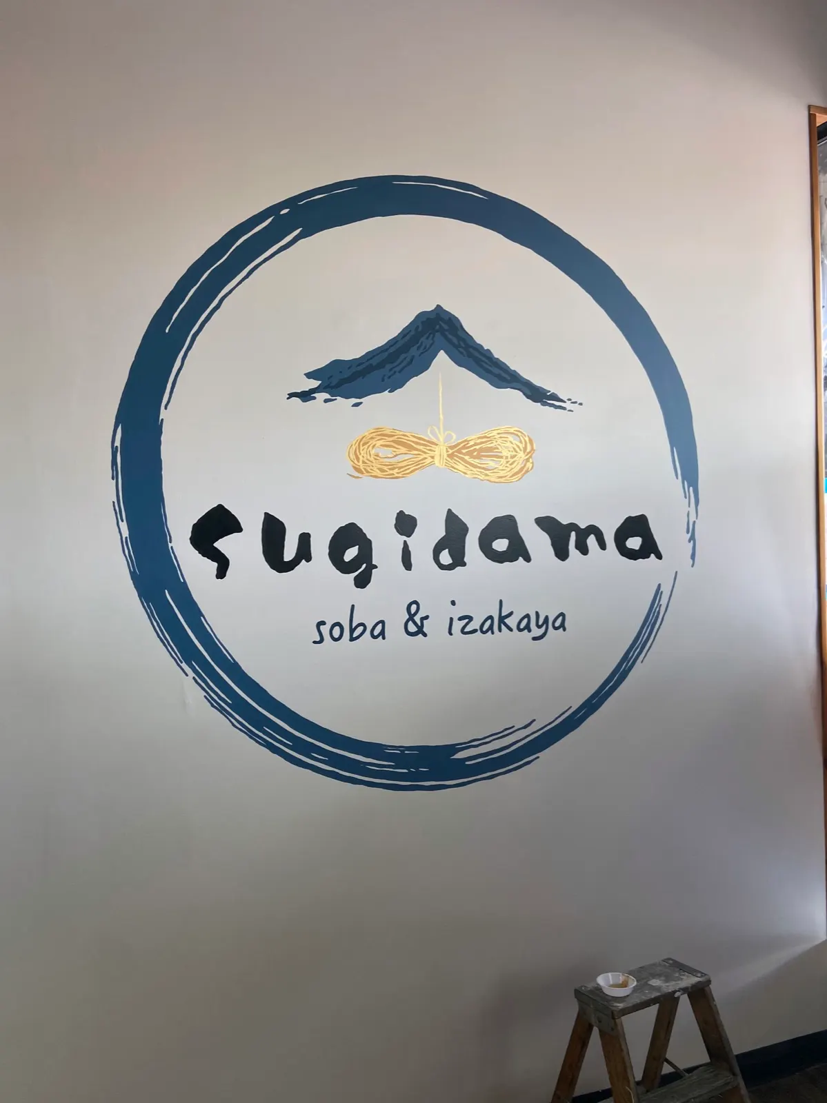 Hand-painted Sugidama Soba and Izakaya logo inside a blue swirl with gold-leaf noodles