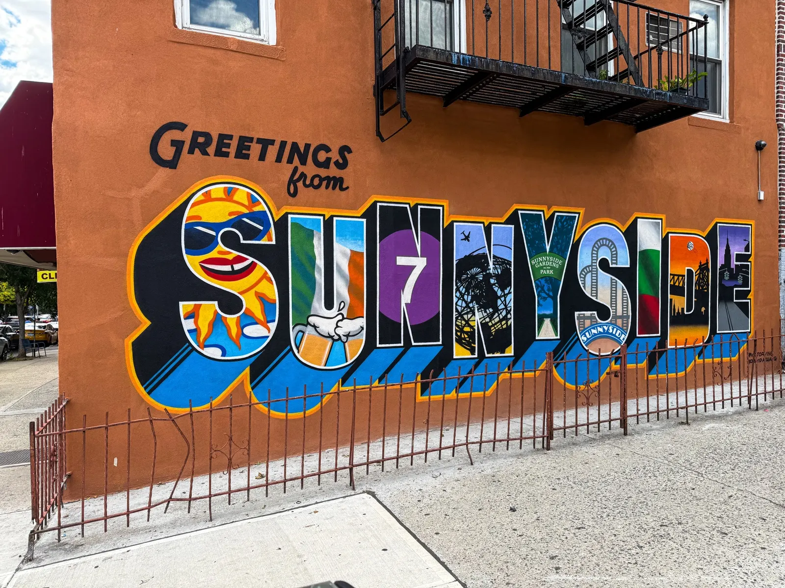 Angled street view of the finished Greetings from Sunnyside mural with Queens landmarks painted inside the letters