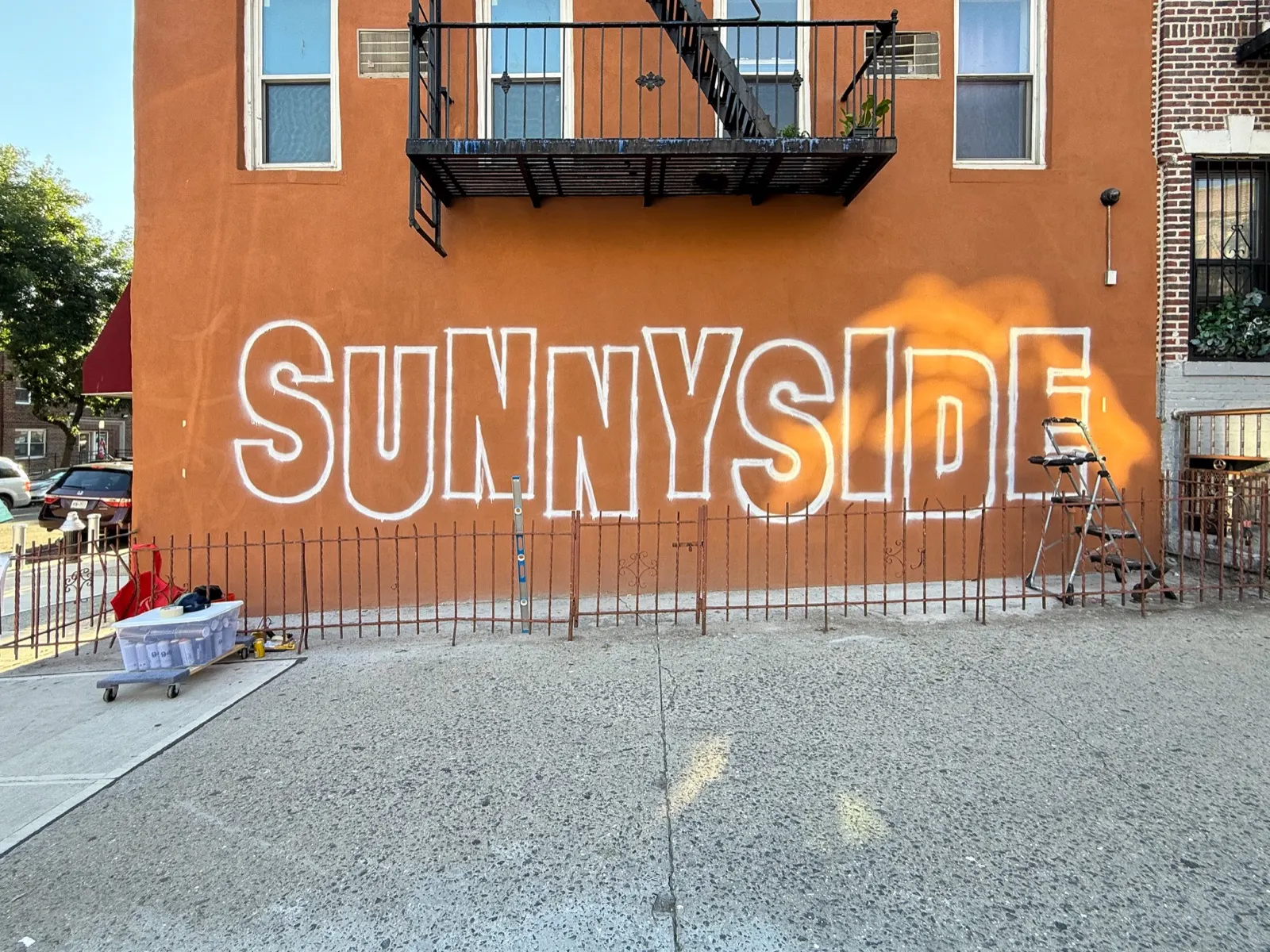 Early daylight stage with Sunnyside outlined across the repaired wall and painting equipment set along the sidewalk