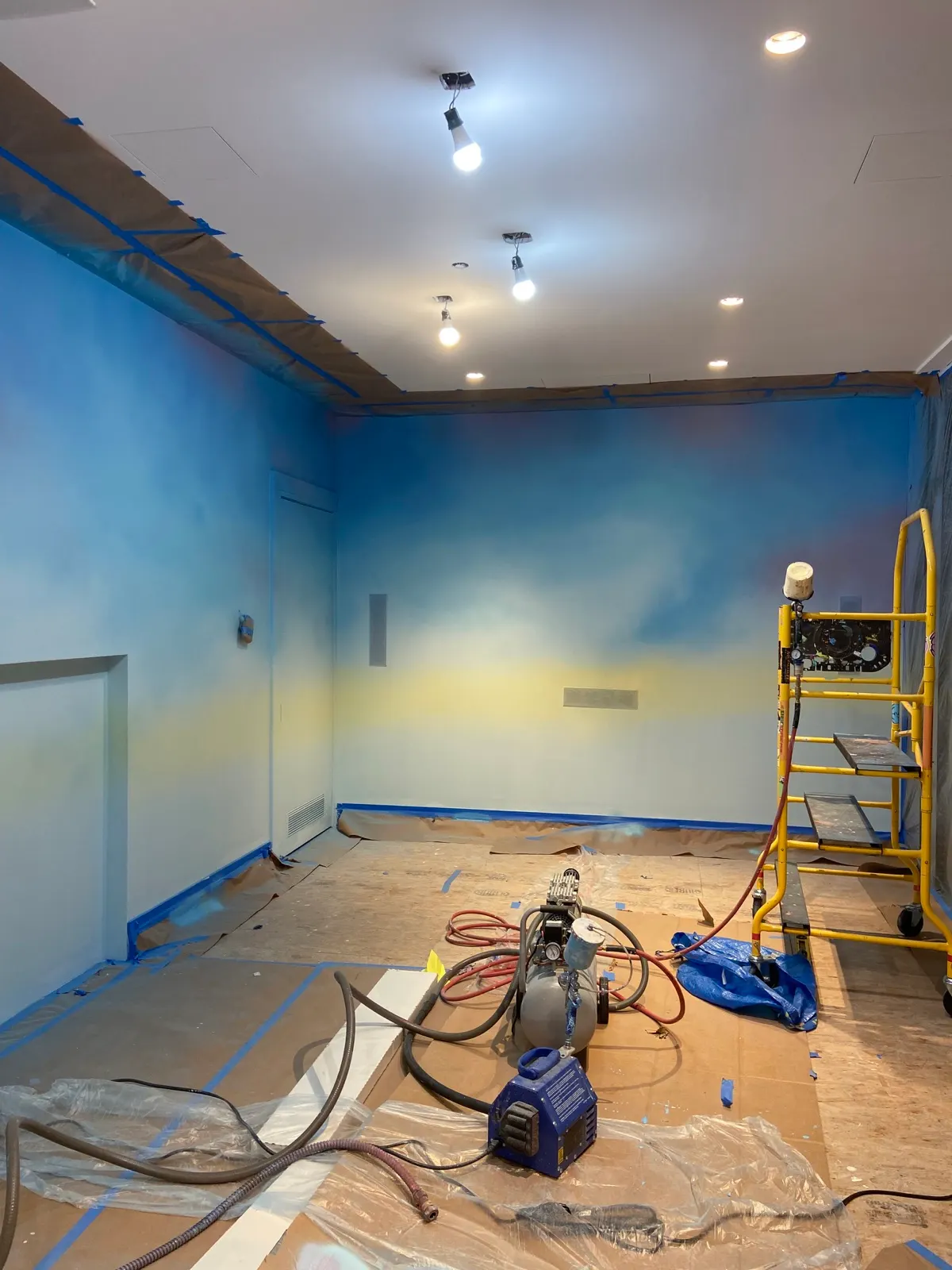 Blue and pastel airbrushed sky taking shape across the Tribeca playroom walls