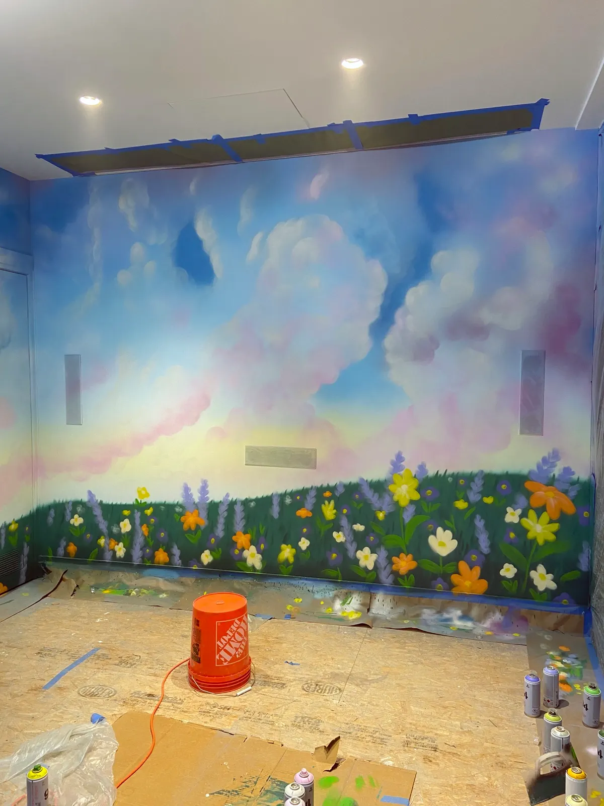 Whimsical cloud and flower mural nearing completion in the main Tribeca playroom