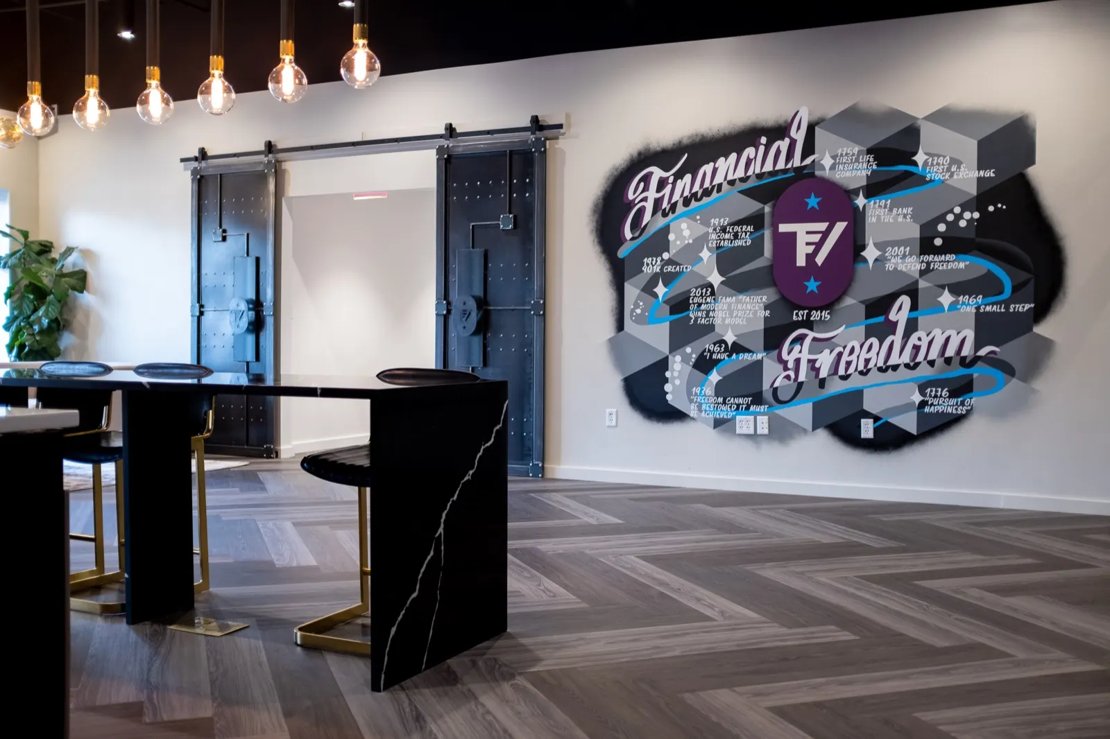 Wide lobby view with the Financial Freedom mural framed by sliding glass doors, a black meeting table, and pendant lights