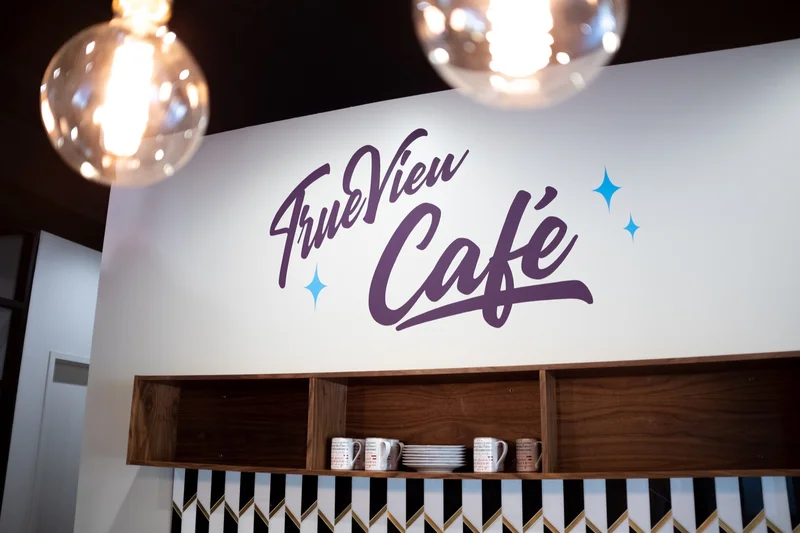 Hand-painted TrueView Cafe script above wood shelving and patterned tile in the office cafe