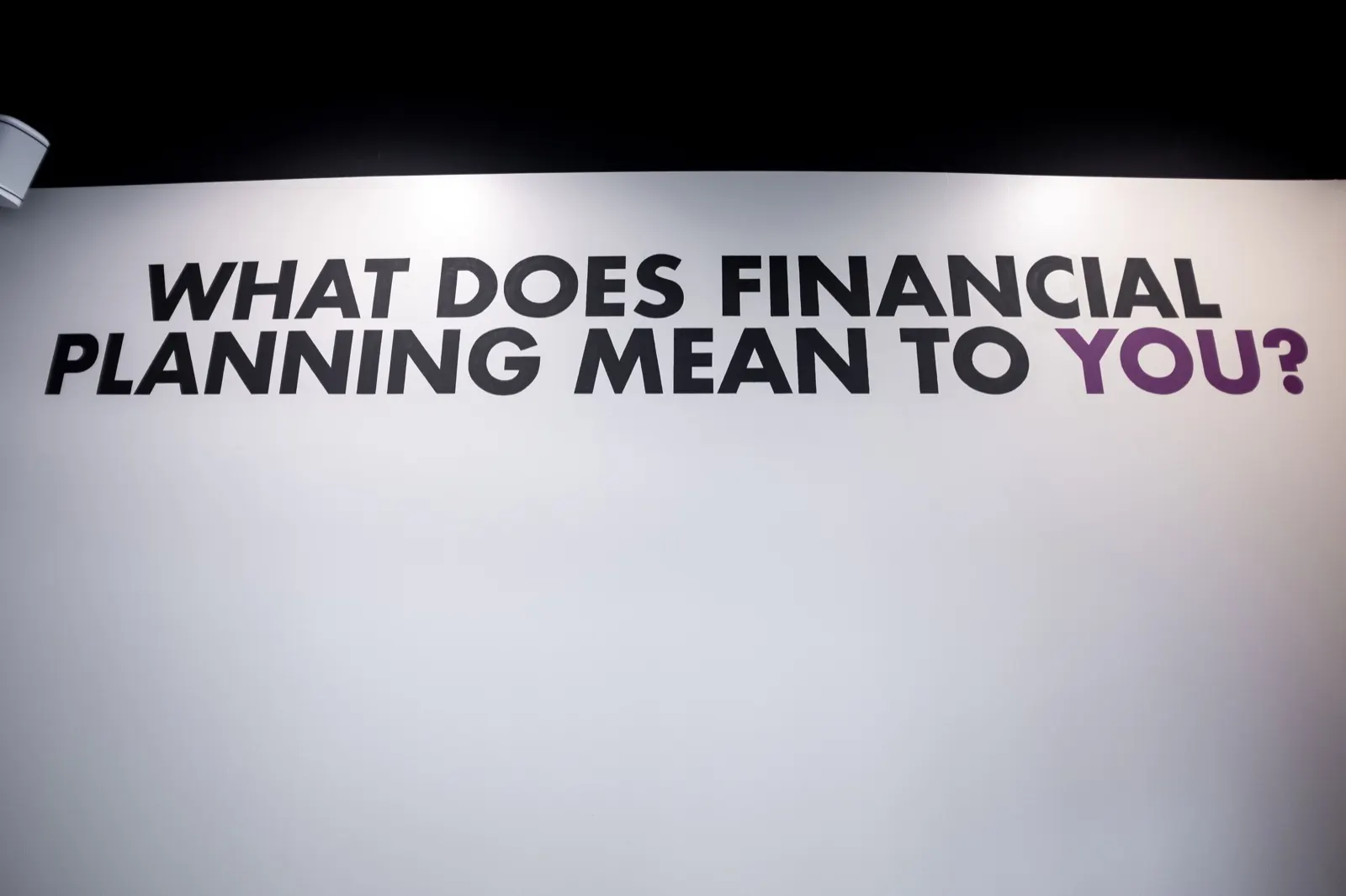 Hand-painted question What does financial planning mean to you in black and purple lettering on a white office wall
