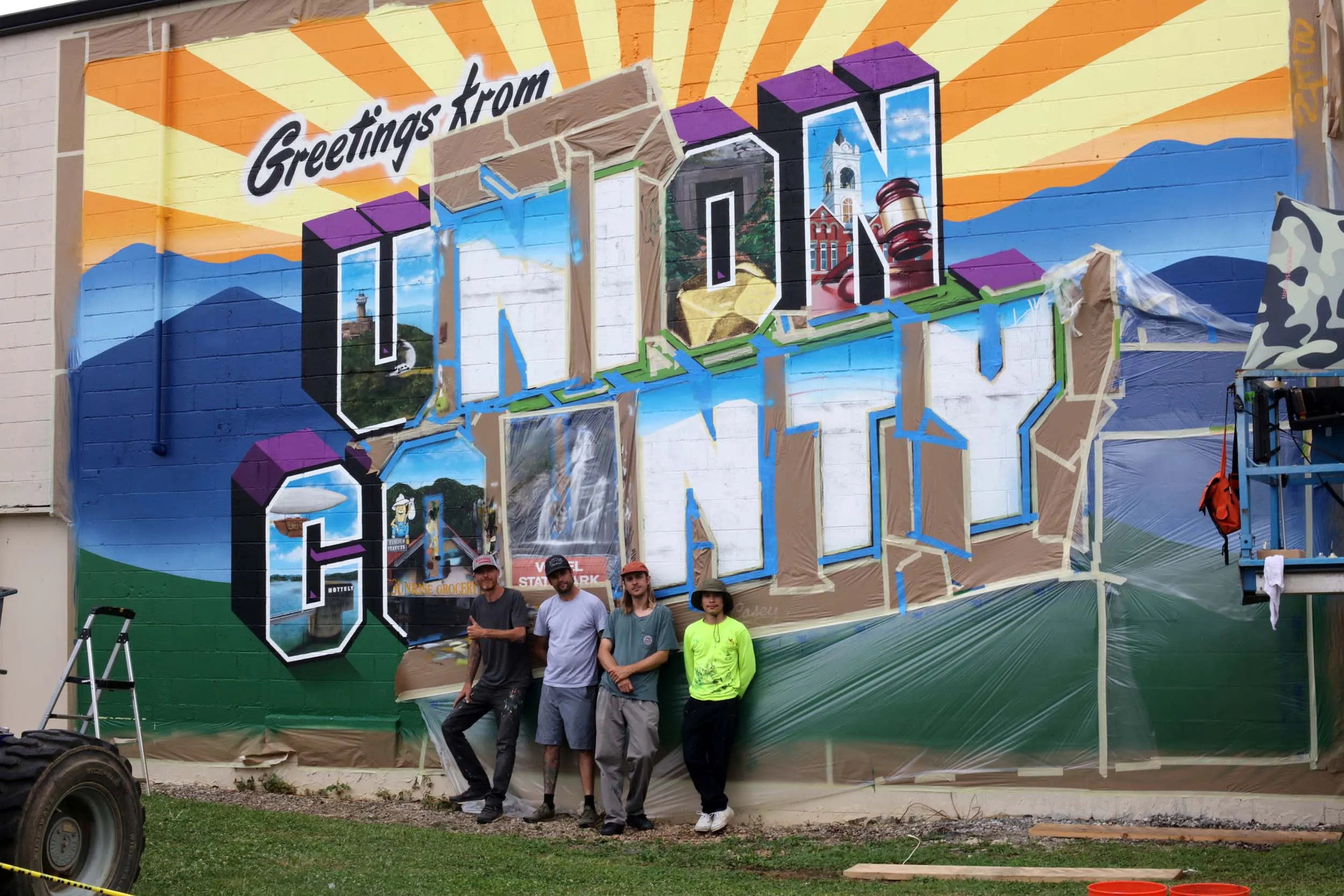 Four-person production team standing in front of the mural in progress