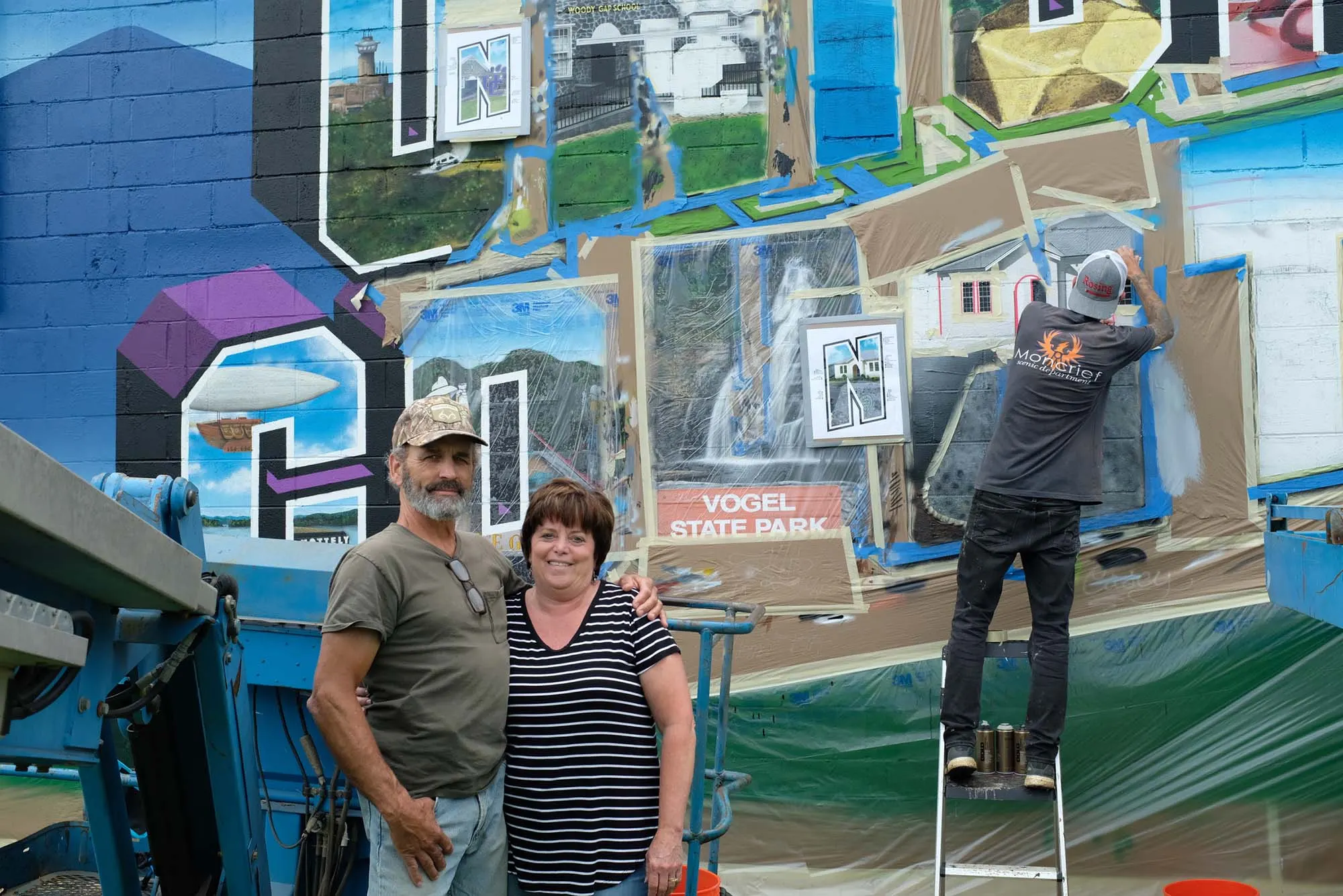 Two Blairsville residents posing while an artist paints from a lift