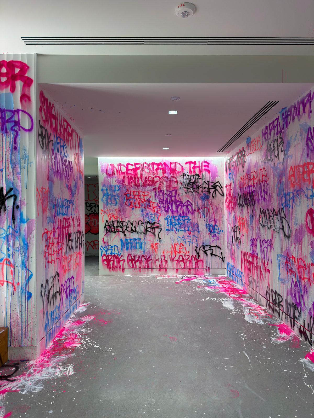 Corridor walls layered with pink, blue, and black graffiti tags at the xAI office