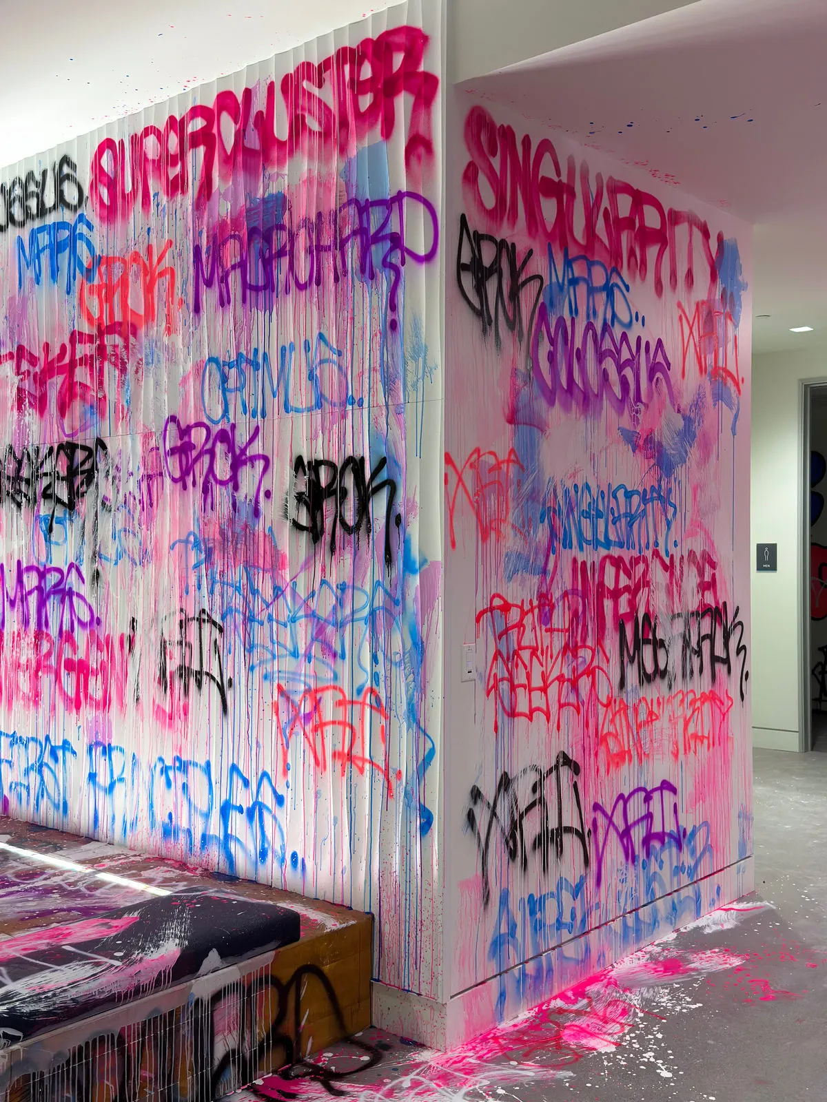 Graffiti wrapping around a white corner wall beside the xAI office entrance