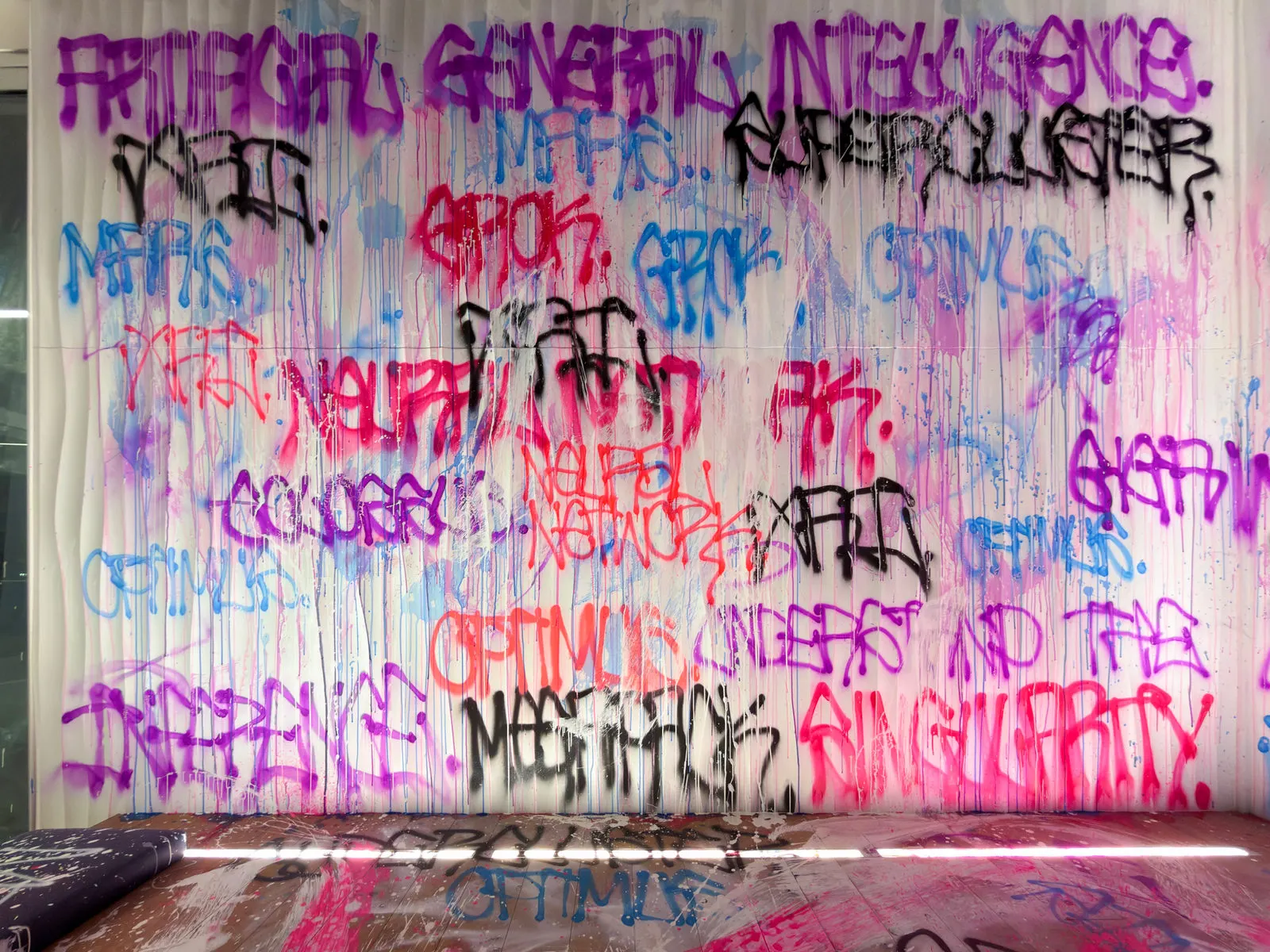 Layered graffiti tags painted across a ribbed white wall and floor